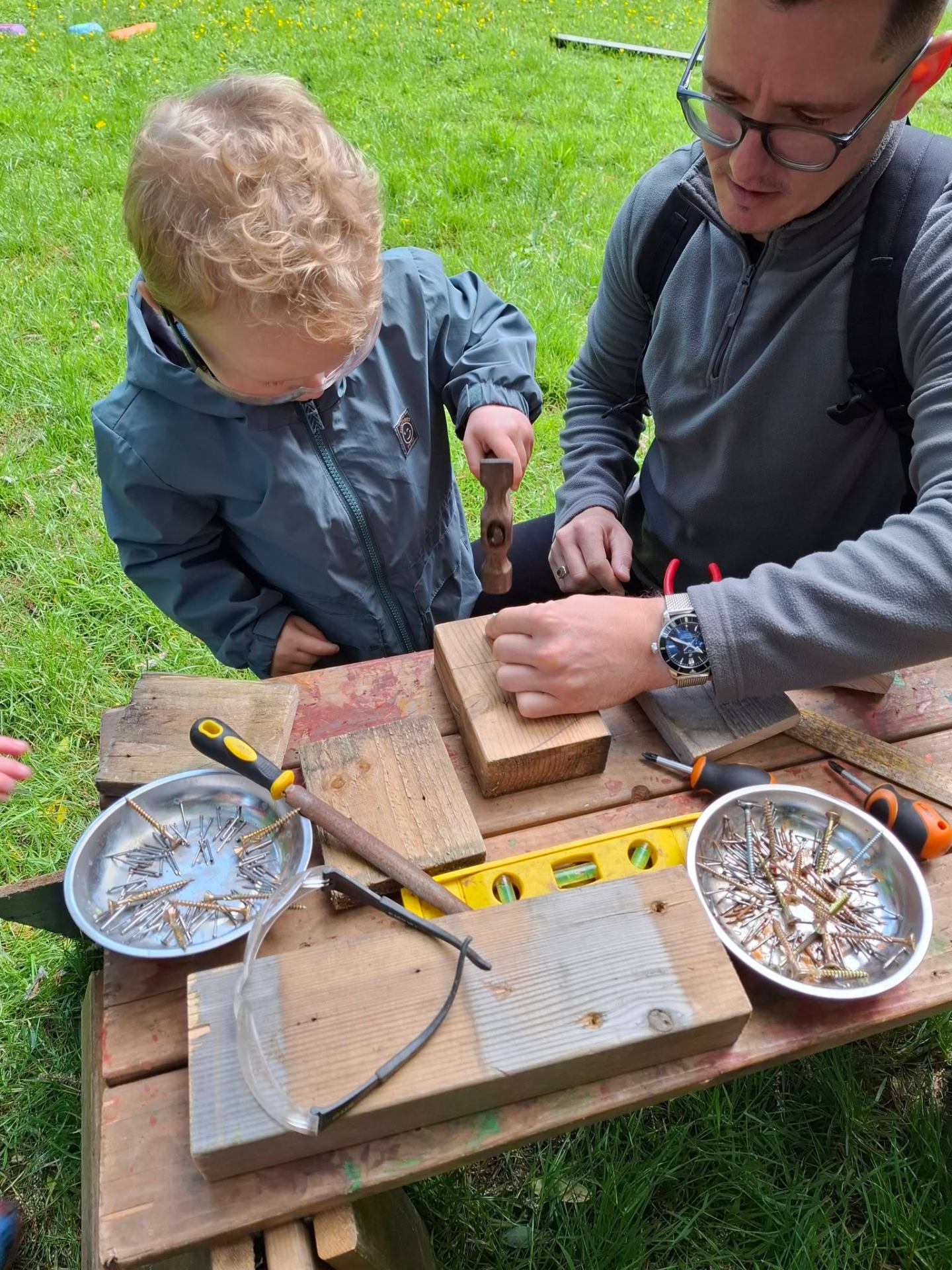 Adult helping a young child use a hammer at the tool station